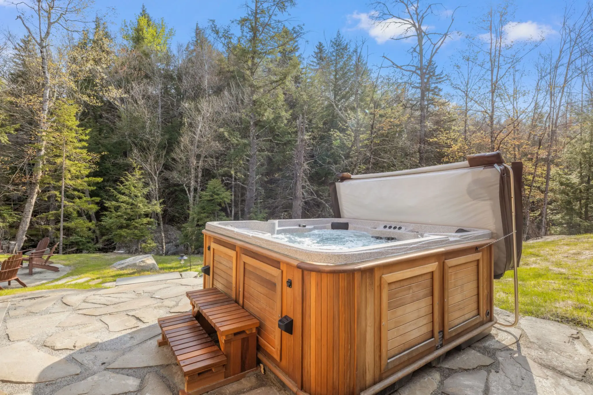A wooden spa on a flagstone patio at the edge of the forest